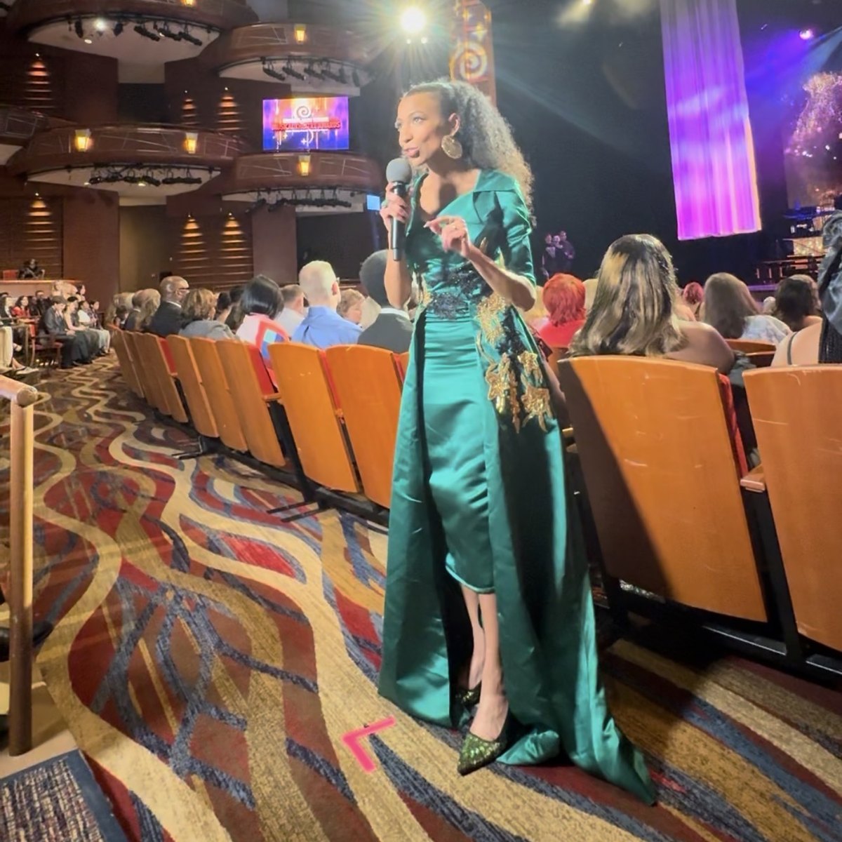Chelsea hosting from the theater aisle in an emerald gown during a live awards broadcast