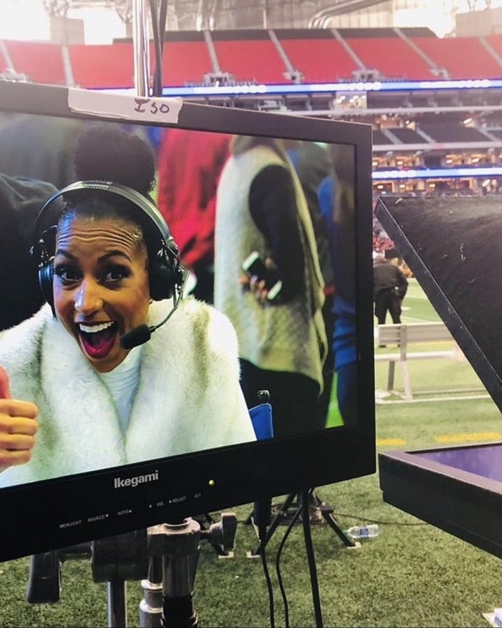 A broadcast monitor showing Chelsea on headset giving a thumbs up from the stadium