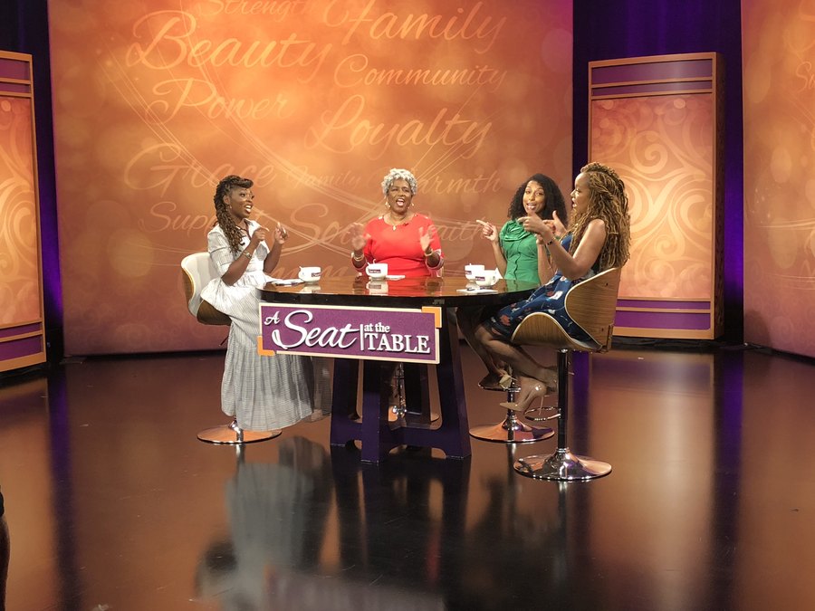 Chelsea in conversation on a talk show set with three other women